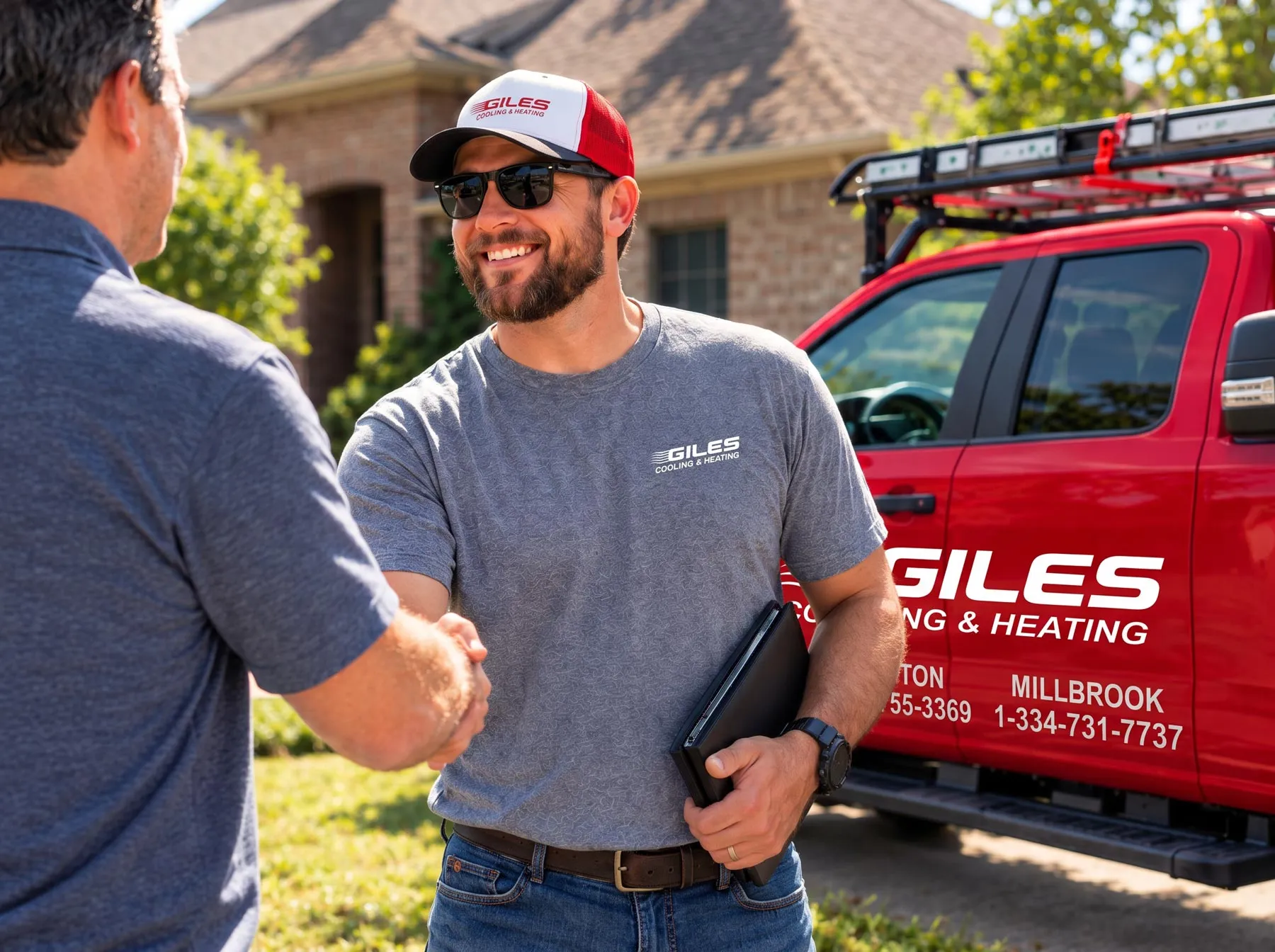 A man in a Giles Cooling & Heating shirt and cap smiling and shaking hands in front of a red service truck.