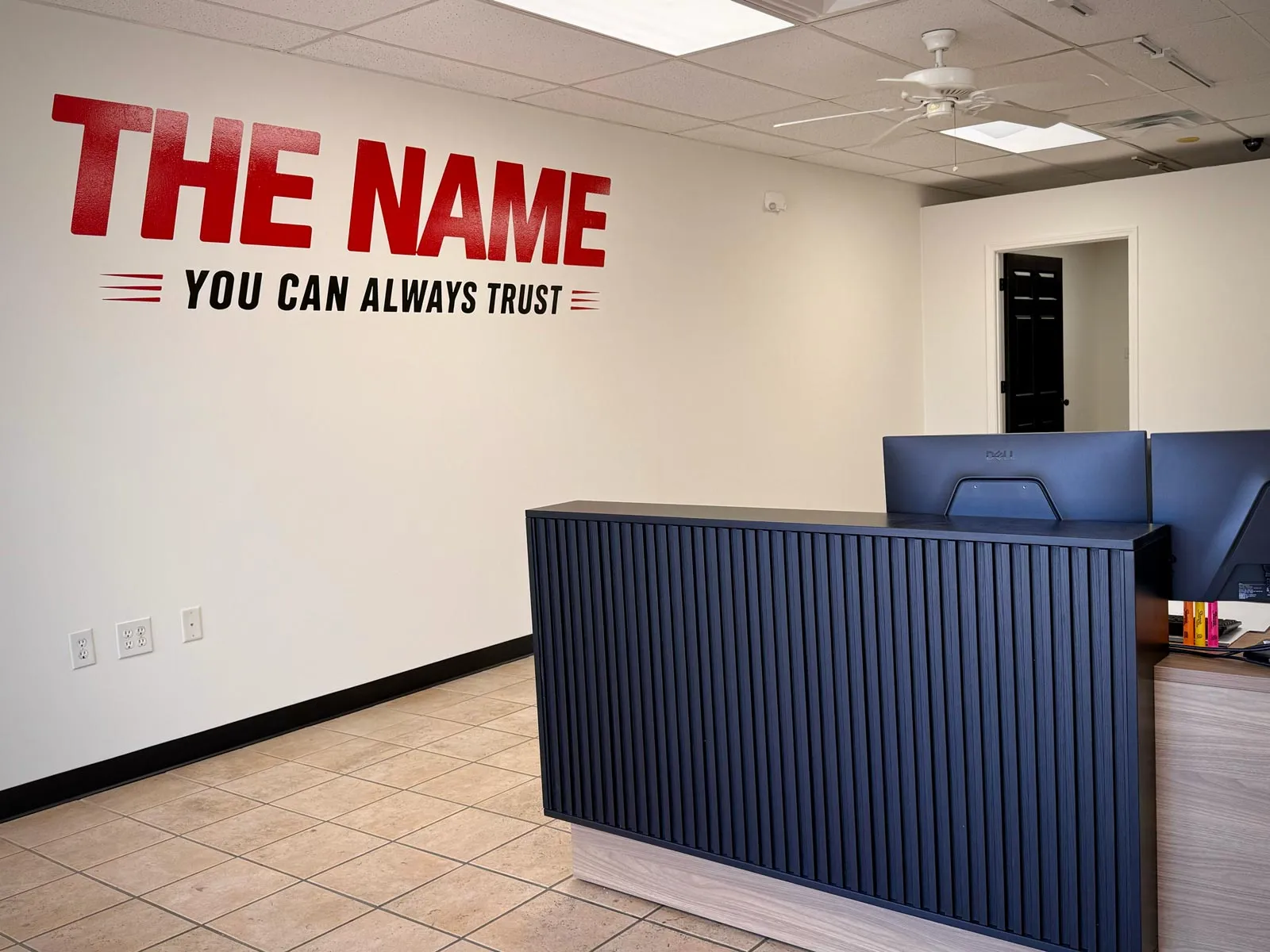 Reception area with navy ribbed desk and wall slogan 'THE NAME YOU CAN ALWAYS TRUST' in red