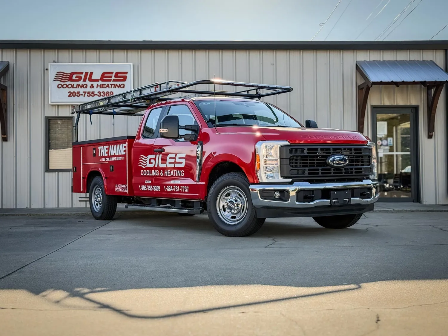 Red Giles Cooling & Heating service truck with ladder rack parked outside company building