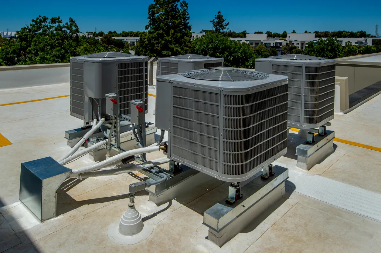 Rooftop air conditioning condensers and HVAC units mounted on a commercial building roof with piping and supports